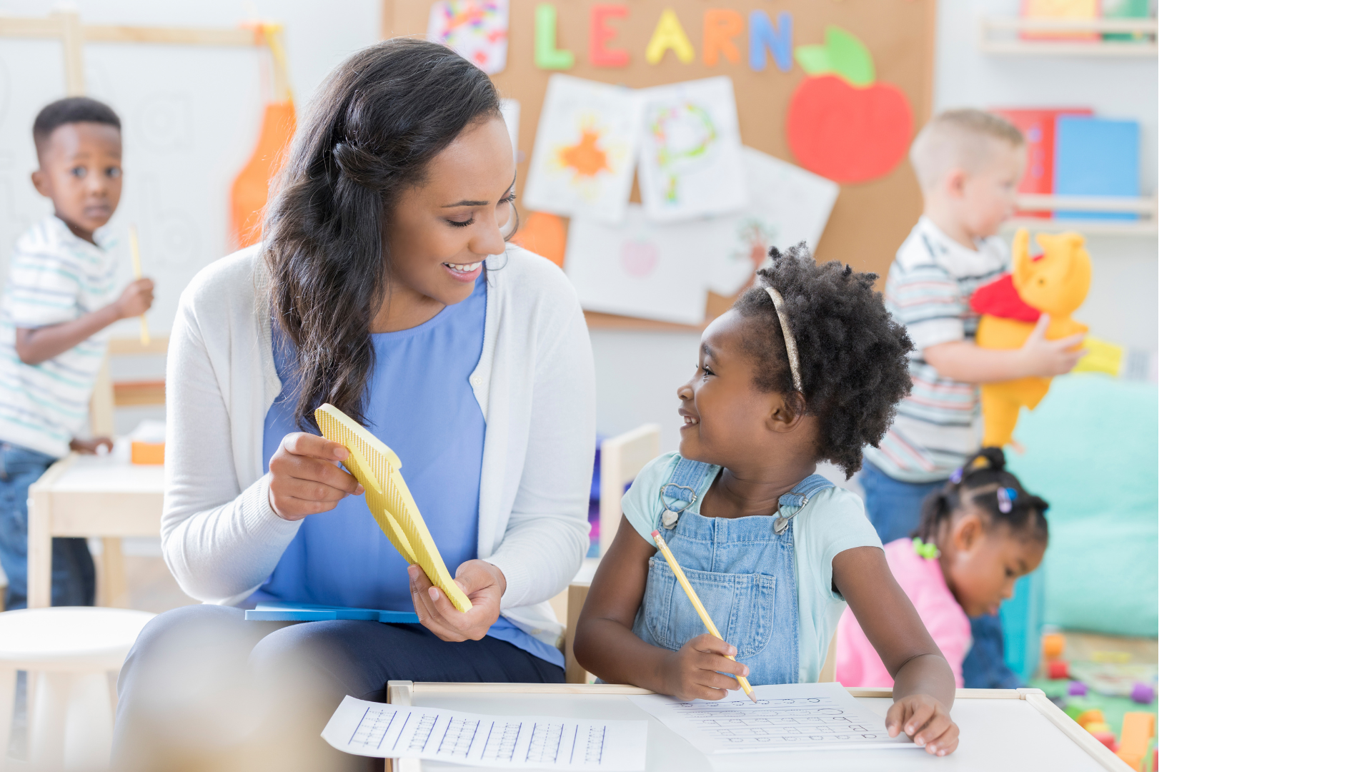 female teacher holding a letter B smiling at small girl child